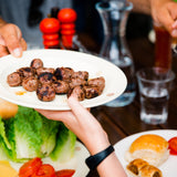 Person holding a plate of grilled meatballs at a table with others