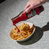 Hand pouring Freddie's Tomato sauce onto a bowl of fries